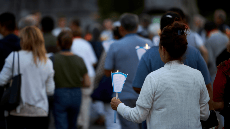 Una pellegrina tiene una fiaccola accesa mentre cammina insieme ad altri fedeli durante la Processione aux Flambeaux di Lourdes.