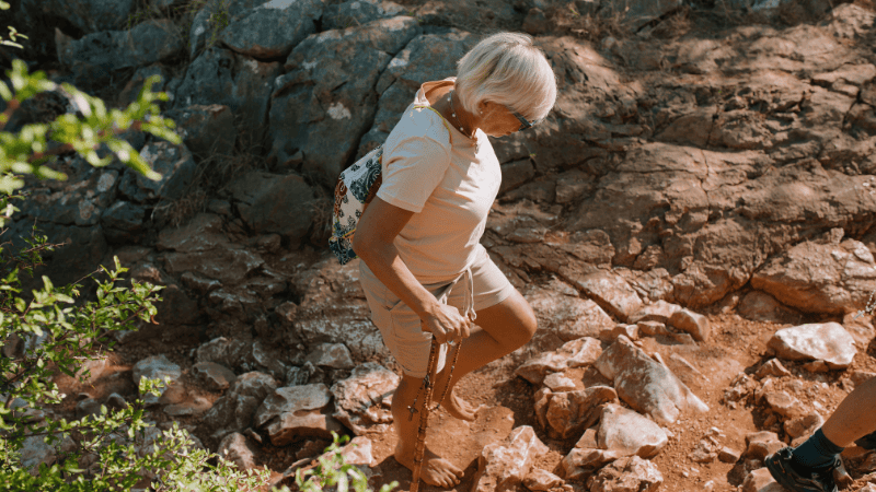 Una pellegrina percorre a piedi nudi il sentiero roccioso di Medjugorje, simbolo di un profondo cammino personale verso la pace.