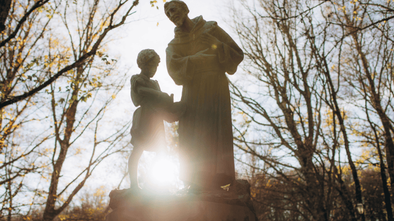 Statua di San Francesco d’Assisi con un bambino nei boschi, simbolo di fede e semplicità lungo i percorsi francescani di pellegrinaggio.