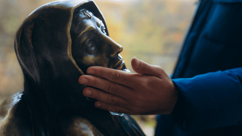 Pellegrino che accarezza il volto della statua di Santa Rita da Cascia, gesto di fede e invocazione di guarigione miracolosa.