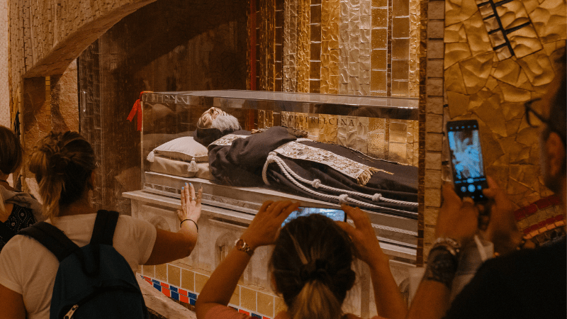 Pellegrini pregano e scattano foto davanti al corpo esposto di Padre Pio nella cripta del santuario di San Giovanni Rotondo.