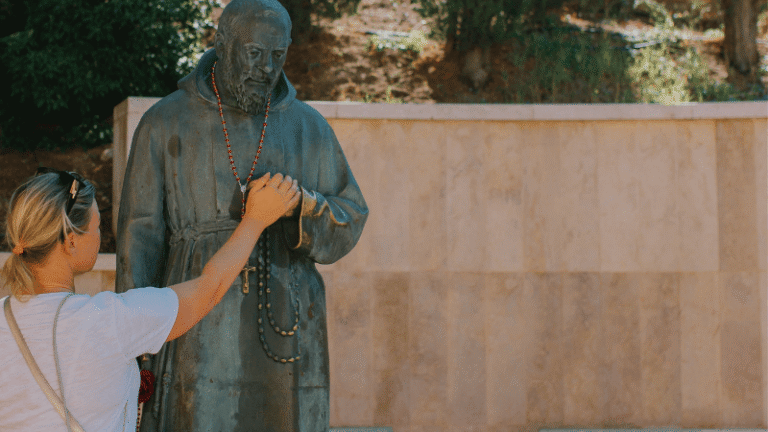 Donna in preghiera accarezza il rosario nella statua di Padre Pio all’esterno del santuario di San Giovanni Rotondo.