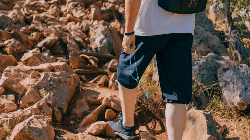 Un uomo cammina sui sentieri di Medjugorje tenendo un rosario, simbolo del cammino di fede e perdono fraterno.