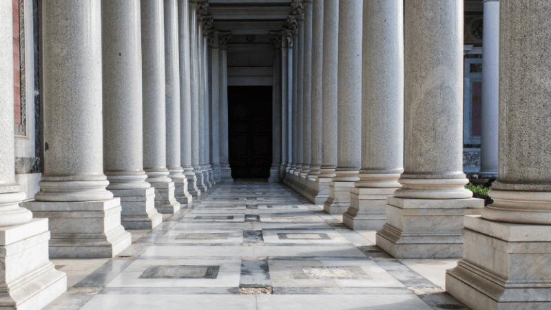 Colonnato maestoso di una basilica romana, luogo di silenzio e raccoglimento per i pellegrini che scoprono la Roma più segreta e spirituale