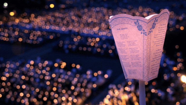 Una fiaccola della Processione aux Flambeaux illumina la notte, simbolo delle preghiere e della fede di migliaia di pellegrini.