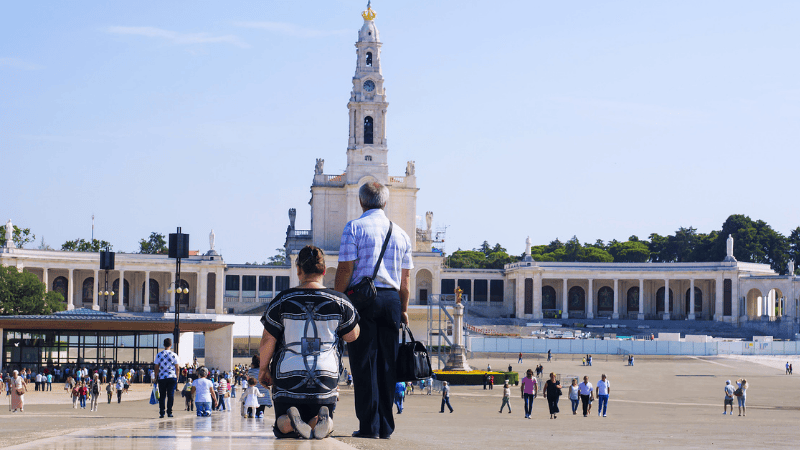 Pellegrini in preghiera, uno dei quali cammina in ginocchio, davanti alla Basilica di Nostra Signora delPellegrini in preghiera, uno dei quali cammina in ginocchio, davanti alla Basilica di Nostra Signora del Rosario nel Santuario di Fatima Rosario nel Santuario di Fatima