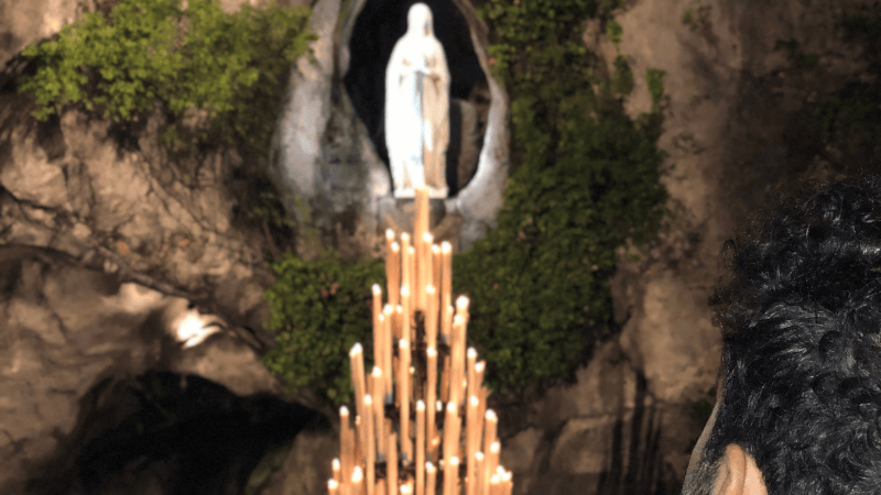 Uomo raccolto in preghiera davanti alla Grotta delle Apparizioni, immerso nel silenzio e nella spiritualità di Lourdes
