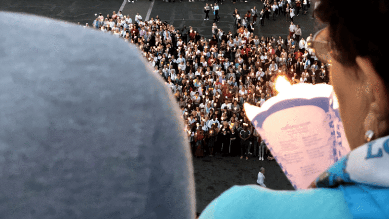 Una pellegrina osserva con emozione la folla raccolta durante la preghiera serale alla suggestiva Processione aux Flambeaux a Lourdes.