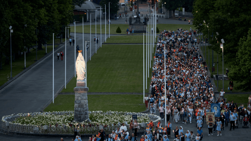 Pellegrini in cammino verso la statua della Vergine Maria durante un intenso momento spirituale a Lourdes