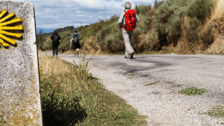 Pellegrini sul Cammino di Santiago a un chilometro dalla meta, accanto alla pietra miliare con la conchiglia gialla simbolo del pellegrinaggio.