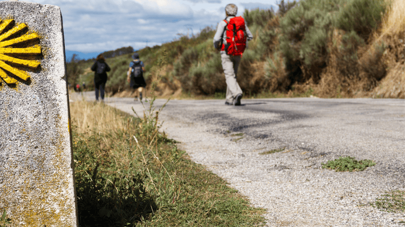 Pellegrini sul Cammino di Santiago a un chilometro dalla meta, accanto alla pietra miliare con la conchiglia gialla simbolo del pellegrinaggio.