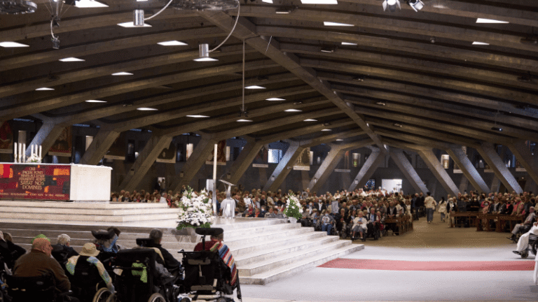 Fedeli radunati nella basilica sotterranea durante la Messa Internazionale di Lourdes, cuore spirituale dei pellegrinaggi.
