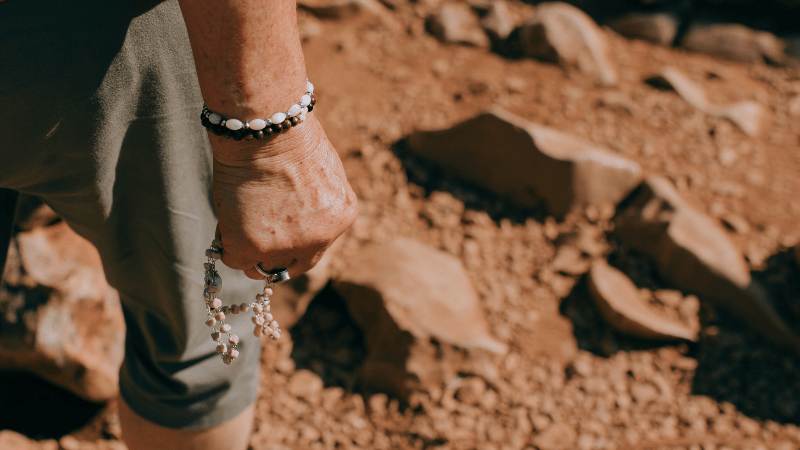 Mano di una pellegrina che stringe un rosario mentre percorre il sentiero roccioso del monte Krizevac a Medjugorje.