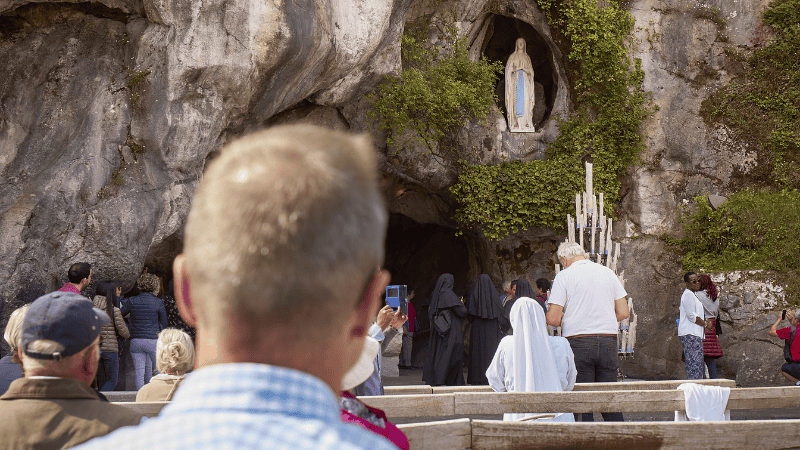 Uomo in contemplazione alla Grotta di Lourdes, luogo delle apparizioni mariane e meta di speranza.