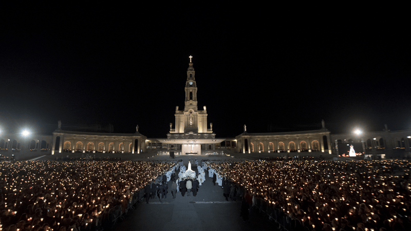 Processione notturna al Santuario di Fatima, con migliaia di pellegrini che tengono candele accese davanti alla Basilica di Nostra Signora del Rosario.