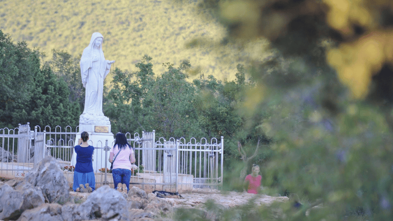 Due pellegrini solitari pregano davanti alla statua della Vergine Maria a Medjugorje, simbolo del viaggio spirituale individuale