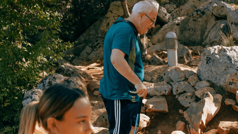 Alfonso sale al Podbrdo di Medjugorje con bastone da trekking tra le rocce della Collina delle Apparizioni durante pellegrinaggio